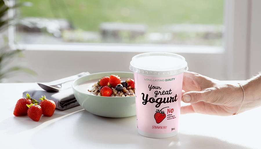 Yogurt in packaging and bowl with strawberries