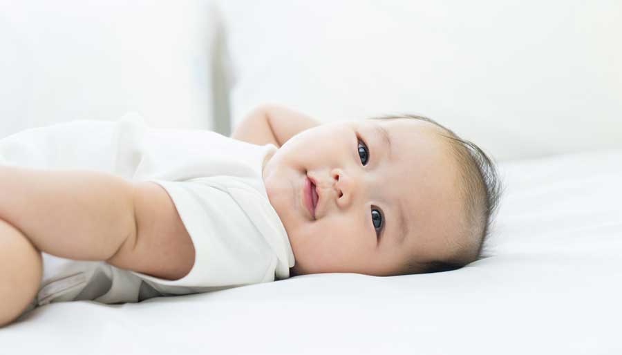 Asian baby laying on white sheets